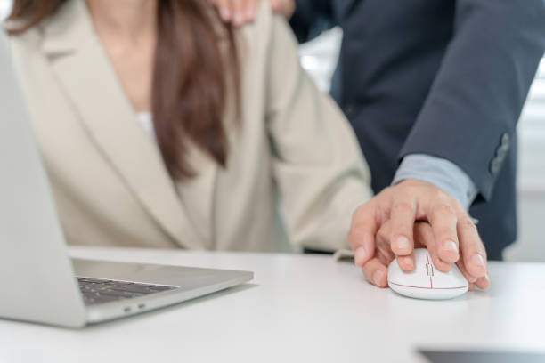 Woman at laptop with hand on computer mouse with man behind her placing his hand on her shoulder and his other hand on top of hers on the mouse.