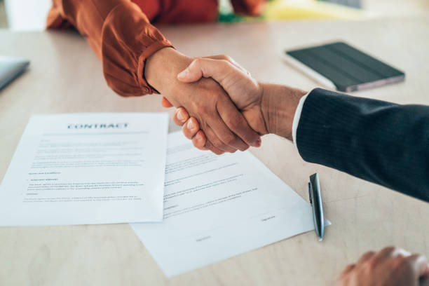 Employer and employee shakings hands from across a table. The table has an employment contract on it.