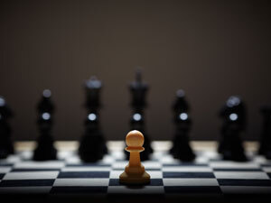 Chess board with single pawn in the foreground alone versus all the opponent's chess pieces in the background